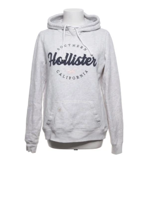 Vit hoodie från Hollister med tryck - Snygg vit hoodie från Hollister med mörkblå logga och texten 'Southern California' på bröstet. Hoodien har huva med dragsko och en stor magficka. Tillverkad i mjukt material som känns skönt mot huden. Perfekt för en avslappnad och trendig look.