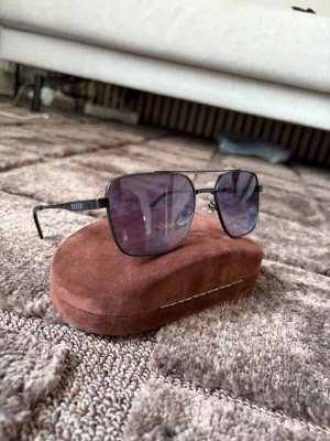 Svarta solglasögon  - Snygga svarta solglasögon med fyrkantiga bågar och mörka glas. Metallbågarna ger en stilren look och glasen har en lätt tonad finish. Perfekta för dig som vill ha en klassisk men modern accessoar. Obs fodralet ingår inte utan endast till för att lyfta fram glasögonen. Finns även guldiga på min sida 