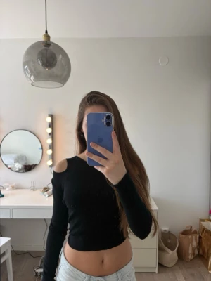 Svart crop top med cut out-detaljer - Trendig svart långärmad crop top med cut out-detaljer på axlarna. Tight passform och rund halsringning. Perfekt för dig som vill ha en edgy och modern look. Materialet ser ut att vara mjukt och stretchigt, vilket gör toppen bekväm att bära.