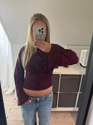 Vinröd croppad topp med vida ärmar - Trendig vinröd croppad topp med långa, vida ärmar och lätt rynkad detalj under bysten. Mjuk och stretchig känsla, perfekt till jeans eller kjol. Enkel och stilren design utan synliga mönster eller loggor.