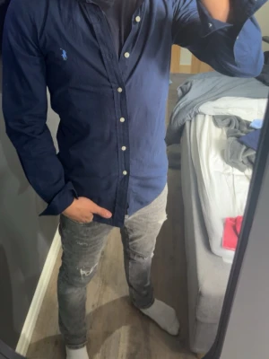 Mörkblå skjorta från Ralph Lauren - Säljer en mörkblå skjorta från Ralph Lauren med klassisk knappstängning och den ikoniska loggan broderad på bröstet. Skjortan har lång ärm och normal passform, perfekt till jeans eller chinos. Materialet känns som bomull och är riktigt skönt.