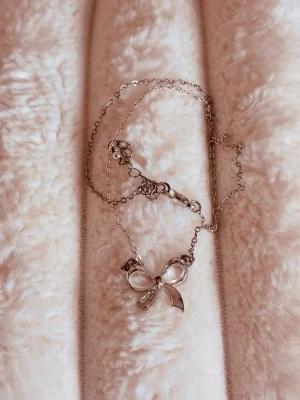 silvrigt halsband & rosett💞 - fint silverfärgat halsband med rosett & glittriga stenar! kedjan är i mycket gott skick men rosetten är pyttelite sliten (missfärgad), men det är absolut inget som syns🩷jag erbjuder bundle rabatter så kolla in mina andra annonser också! de är bara att höra av dig vid frågor eller prisförslag🌺