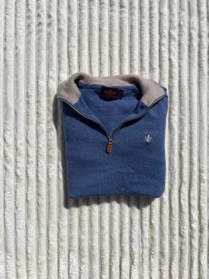 Blå halvzip tröja från Morris - Blå långärmad tröja från Morris med halvzip och beige krage. Tröjan har en liten broderad logga på bröstet och förstärkta armbågar. Perfekt för dig som gillar klassisk stil med en twist.