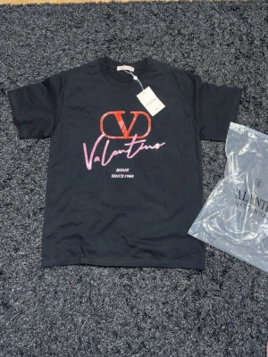 Svart Valentino t-shirt med tryck - Snygg svart t-shirt från Valentino med stort rött och rosa logotryck framtill. Klassisk rund hals och korta ärmar. Tillverkad i mjuk bomull för skön känsla. Perfekt för dig som vill ha en statement-tee med exklusiv känsla.