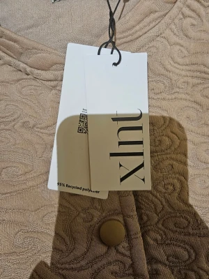 Beige quiltad cardiganjacka från Lindex - Stilren beige cardiganjacka från Xhll med quiltat mönster och rund halsringning. Jackan har knappar framtill och är tillverkad av 95% återvunnen polyester. Perfekt för dig som gillar en enkel men trendig look.