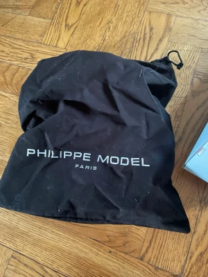 Svart dustbag Philippe Model Paris - Säljer en svart dustbag från Philippe Model Paris. Påsen är tillverkad i tyg och har dragsko upptill. Perfekt för att förvara eller skydda dina väskor eller skor. Märkets logga är tryckt i vitt på framsidan.