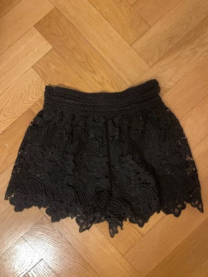 Svarta spets-shorts med blommönster - Snygga svarta shorts med bred resår i midjan och detaljerad spets med blommönster. Shortsen är vintage och därför står det inte storleken men passar som 36/38! Finns ett hål inuti men syns inte. Säljer för 450kr då jag köpte för mycket dyrare! ❤️