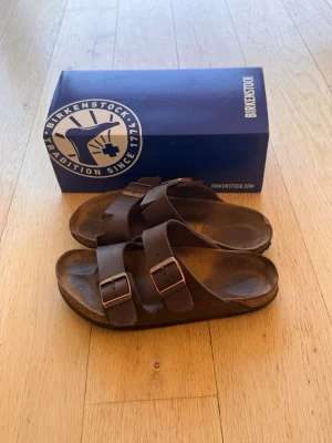 Birkenstock arizona 40 - Säljer dessa Birkenstock arizona i stl 40. De är väl använda och köpte 2025 april. De är väl använda och försökt tagit hand om dem så mycket som det gått men har inte varit lätt. De har varit i ett hundfritt hem men en kompis hund har käkat lite på ena tofflan. Hör av er vid funderingar 