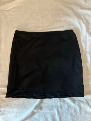 Svart enkel kortkjol - En basic svart kortkjol med rak passform och resår i midjan. Kjolen är gjord i ett mjukt material som känns bekvämt mot huden. Perfekt att matcha med en crop top eller hoodie för en clean look.
