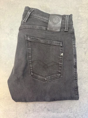 Svarta jeans Replay Anbass, stl 33/31 - Snygga svarta jeans från Replay med klassisk femficksmodell och raka ben. Jeansen har en diskret logga på bakfickan och patch i läder vid linningen. Tillverkade i mjukt denimtyg som ger en skön passform och stilren look.