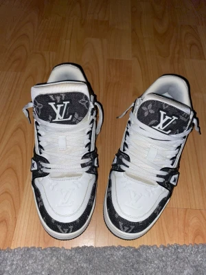 Skor vita och svarta sneakers - Snygga sneakers i vitt och svart med klassiskt monogram på tungan och detaljer runt skon. Skorna har högt skaft, vita snören och är tillverkade i en mix av läder och textil. Perfekta för dig som vill sticka ut med exklusiv streetstyle.