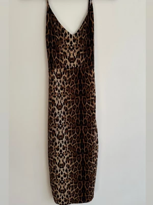 Leopardmönstrad långklänning - Säljer en snygg leopardmönstrad långklänning med smala axelband och v-ringning både fram och bak. Klänningen har en figurnära passform och är perfekt för dig som vill sticka ut. Materialet känns mjukt och följsamt, troligen polyester. 