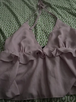 Ljuslila volang topp med knyt - Supersöt ljuslila topp med volangdetalj och knyt i nacken. Toppen är ärmlös och har en luftig, croppad passform som passar perfekt till sommaren. Materialet känns lätt och flowy, perfekt för varma dagar.