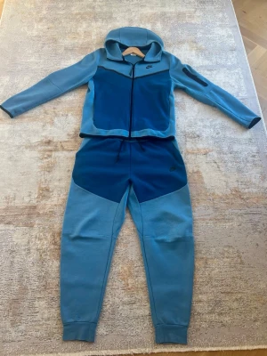Blå Nike tech fleece  - Säljer en Tech Fleece som tyvärr inte kommer till användning längre. Setet är endast använt ett fåtal gånger och är i mycket fint skick, i princip som nytt.  Tröjan är i storlek M och byxorna i storlek L.  Pris kan diskuteras vid snabb och smidig affär. Hör gärna av dig vid intresse eller om du har några frågor!