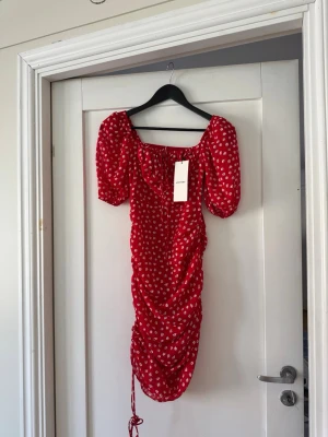 Röd blommig klänning från Adoore - Supersöt röd klänning från Adoore med vita blommor, puffärmar och snörning vid urringningen. 