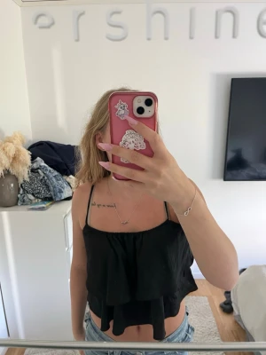 Svart croppad linnetopp från H&M - Säljer en svart croppad linnetopp från H&M med tunna axelband och dubbla lager tyg som ger en flowy look. Perfekt till jeans eller kjol för en chill och trendig stil. Toppen är ärmlös och har en loose passform.