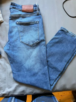 Blå raka jeans från Jack and Jones - Säljer ett par klassiska blå jeans från Jack and Jones med raka ben och fem fickor. Jeansen har normalhög midja och är gjorda i ett mjukt denimtyg med snygg tvätt och kontrastsömmar. Perfekta till en avslappnad stil.