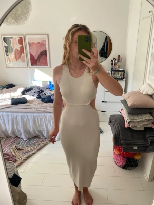 Krämvit ribbad långklänning med cut-outs - Trendig krämvit långklänning i ribbat material med cut-outs i midjan och rund halsringning. 