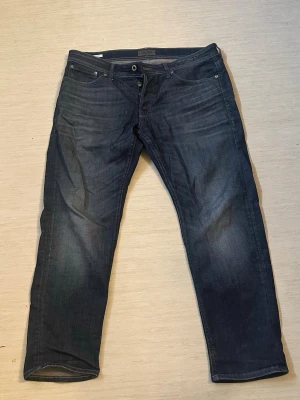 Mörkblå jack and jones jeans - Snygga mörkblå jeans med raka ben och dubbla knappar i midjan. Klassisk femficksmodell med diskreta slitningar och kontrastsömmar. Jeansen har en stilren look och passar perfekt till en avslappnad outfit. Köpta för 800 ny pris, 34 midja 30 längd