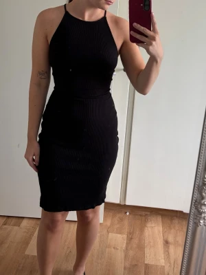 Svart ribbad kort klänning från H&M - Säljer en svart ribbad kort klänning med smala axelband och öppen rygg med snörning. Klänningen har en tight passform och är perfekt för dig som gillar en enkel men snygg stil. Materialet känns mjukt och följsamt.
