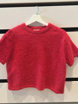 Röd stickad t-shirt Gina Tricot - Kortärmad stickad t-shirt i en härlig röd färg från Gina Tricot. Tröjan har rund halsringning med ribbad kant och är gjord i ett mjukt, fluffigt material som känns skönt mot huden. Perfekt för dig som vill ha en trendig och bekväm look. Tröjan är oanvänd.