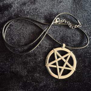 Nytt halsband med silverfärgat pentagram i rostfritt stål, band i konstläder.   Ovanligt och stilrent.  Amuletten är 5 cm lång och 4,5 cm bred, halsbandet är cirka 60 cm långt med 5 att justera med. Låses med hummerlås.   Unisex. 