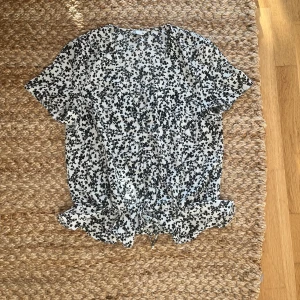 Blus - Bjud med någon typ av dragsko i mitten, vilket gör att man kan dra ihop den. V- ringad men syns inte jättetydligt på bilden. Resår och volang i midjan.👚