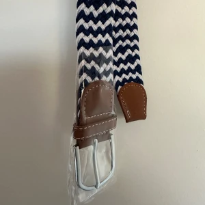 Flätat bälte - Bältet är i mycket bra skick och helt oanvänt det är också riktigt snyggt. Färgerna på bältet är blått och vitt i skicksack mönster.