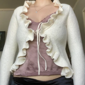 Stickad kofta med volanger - Stickad kofta med volanger, créme vit i färg. Passar XS/S