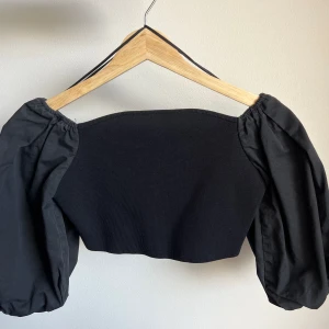 Svart topp med puffarmar - En jättegullig kort svart topp med puffarmar från Zara i storlek S. Den har bara använts 2 gånger och är som en helt ny☺️  Det går även att ha den som off shoulder✨ Skriv till mig om du har frågor eller vill ha närmare bilder på toppen😊