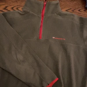 Fleece tröja - As mysig fleece tröja med röda detaljer. Går att justera storleken lite längst ner med hjälp av några spännsaker