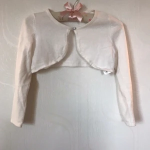 Vit bolero - Fin bolero med diamant knapp. Hade passat bra om man hade en basic enfärgad linne eller T-skirt under boleron. Storleken 122-128. Den är i ganska bra skick. 