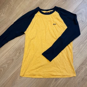 Superdry raglantröja - Raglantröja i gult och mörkblått från Superdry. Oanvänd.