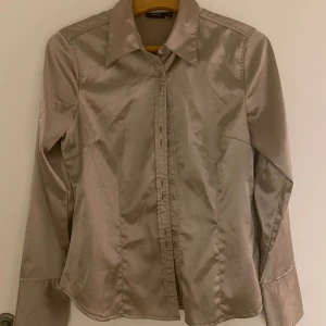 Metallic skjorta/blus - Snygg skjorta/blus i metallic/guldigt tyg. Figursydd så väldigt snygg passform och nice detaljer. 