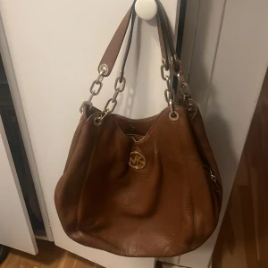 Michael kors väska - Väldigt fin väska äkta Michael kors brun/orange läder. Passar till massa grejer väldigt stort utrymme. Nytt pris 4000