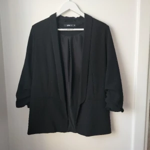 Öppen svart kavaj med rynkade "uppkavlade" ärmar - Storlek 38/M. Funkar om man som S vill ha lite oversize (jag har kört på det). Fint skick!
