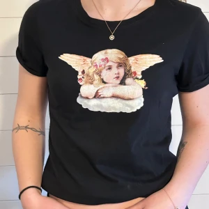 T-shirt  - En svart T-shirt med tryck av en ängel. Sparsamt använd och inga tecken på användning 