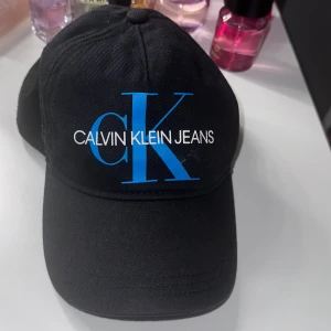 Calvin Klein keps - En svart Calvin Klein keps med blått tryck(säljs inte längre) har används vårdsamt och är i mycket bra skick. Storlek S/M men går att justera storleken bak på kepsen. Hör av er vid frågor. Nypris 599