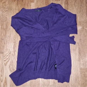 Lila kofta - En lila kofta med långa ärmar och knappar framtill. Koftan har en enkel design och är tillverkad i ett mjukt material.