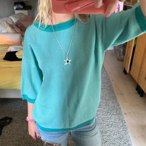 Turkos stickad tröja med gröna detaljer - Säljer en superfin turkos stickad tröja med gröna detaljer vid halsringningen, ärmsluten och nederkanten. Tröjan har trekvartsärmar och en normal passform! 