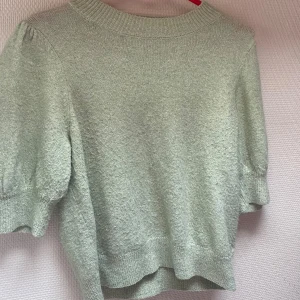 Ljusgrön tröja från Vero Moda - En ljusgrön tröja från Vero Moda med korta ärmar och ribbstickade muddar vid halsen och nederkanten. Tröjan har en mjuk och bekväm textur.