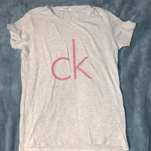 Säljer en snygg grå t-shirt från Calvin Klein med rosa 'ck' logga på framsidan. T-shirten är i bomull och har en normal passform. Perfekt för vardagsbruk!