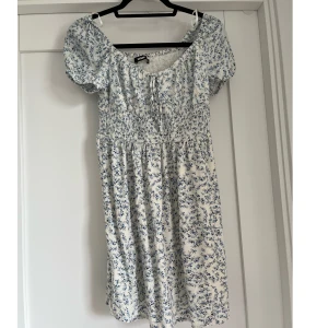 Blommig kort klänning - Somrig vit klänning med blåa blommor som mönster. Klänningen gör att ha som off shoulder eller med armarna upp. Endast använt vid 2 gånger