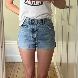 Snyggt slitna jeansshorts från Zara - Säljer ett par snygga blå jeansshorts från Zara i storlek 34. De är högmidjade och har en normal passform. Shortsen har en klassisk femficksdesign och och är lite slitna för en cool look. Ett måste varje sommar! Mått: 33 cm tvärs över midjan. 