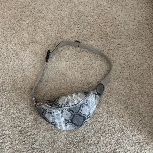H&M magväska - Grå mönstrad magväska i gott skick. Lite sliten vid dragkedjan men annars fin. Man kan justera längden på badet och har ett knäppe som gör den lätt att ta av.💗