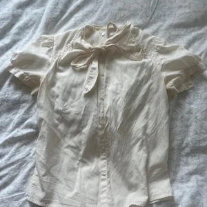 Filippa K blus - Jättesöt crémevit blus från Filippa K med knytning vid kragen och knappar vid ärmarna! ❣️