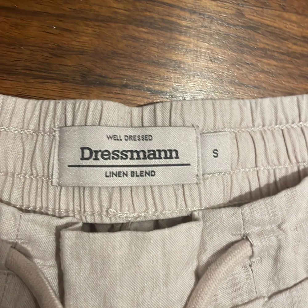 Säljer ett par bekväma beige shorts från Dressmann i storlek S. De är gjorda av en linneblandning och har en elastisk midja med dragsko för justerbar passform. Shortsen har två sidofickor och två bakfickor med knappar. Perfekta för varma sommardagar!. Shorts.