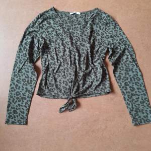 En militärgrön tröja med svarta leopardprickar, knytdetalj på magen. Storlek 38 från About You. Använd några få gånger, fint skick. Mjukt, behagligt tyg.