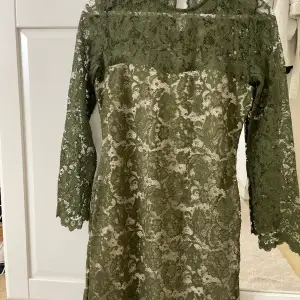 En kort figursydd spetsklänning från Guess.  Färg: olivgrön spets och beige underdel.  Storlek S  Sitter väldigt fint på och är använd endast en gång. Väldigt fint skick! 