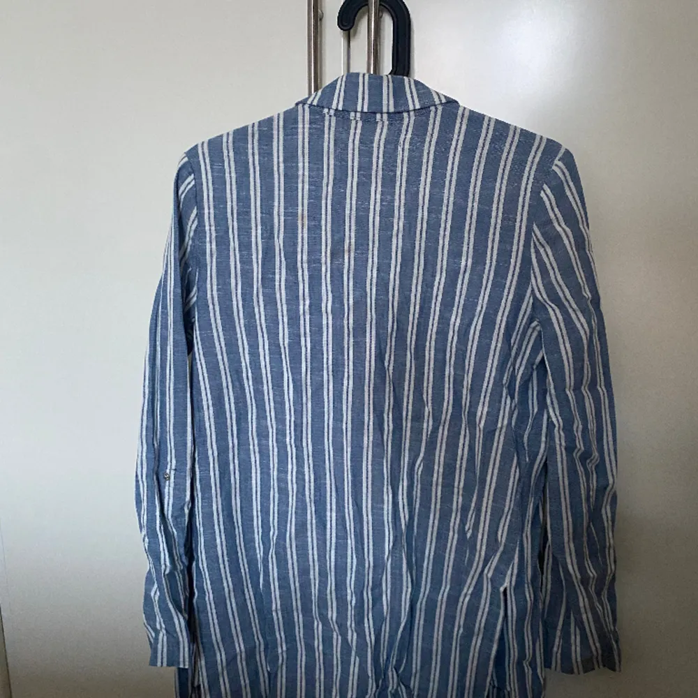 En blå och vit randig kavaj med slits på båda sidor samt fickor. Från märket Stradivarius i storlek S. Puvut & Bleiserit.